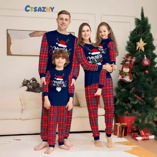Family of four by the Christmas tree in matching navy and red plaid Merry Christmas pajamas